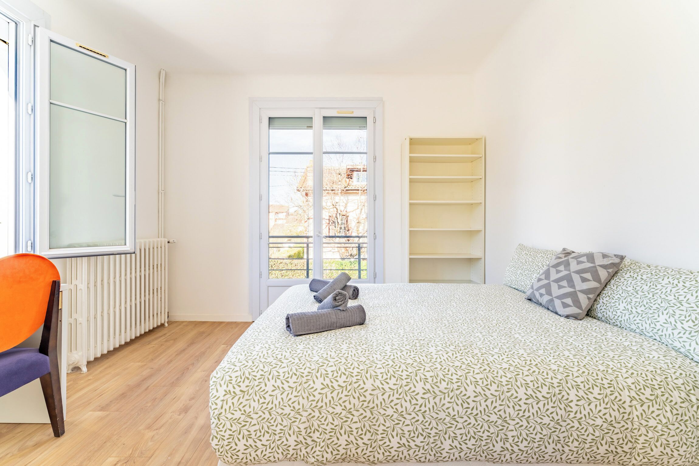 Ein Schlafzimmer mit Bett, Stuhl, Heizkörper, Fenster und Tür.