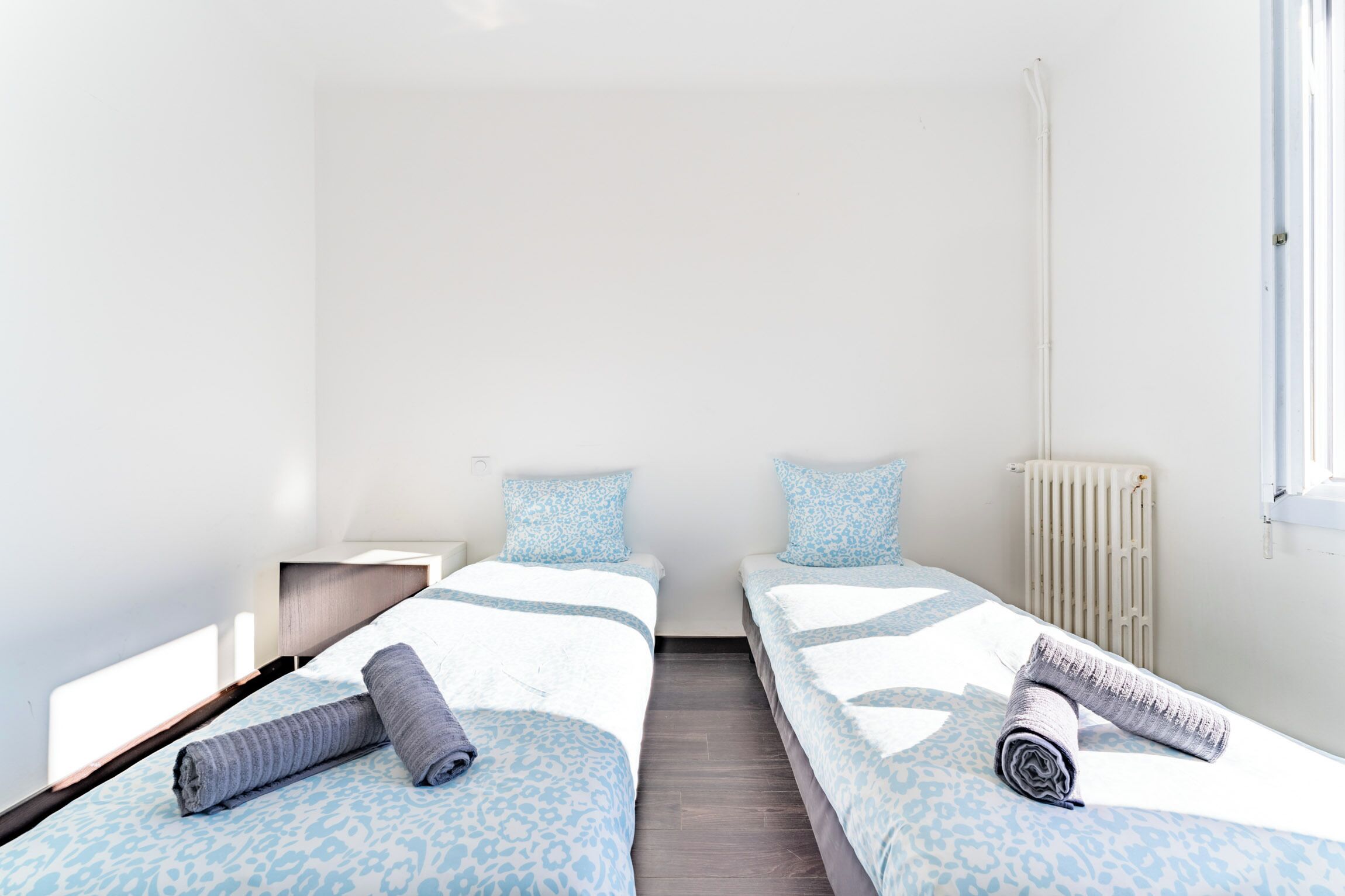 Une chambre double avec deux lits, une table de chevet, un radiateur et une fenêtre.