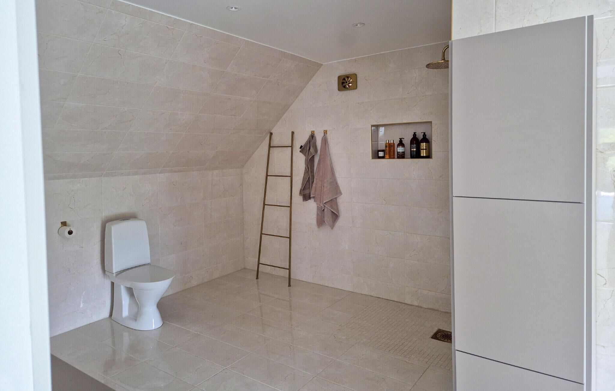 Een badkamer met toilet, douche, handdoekhouder en een plank met toiletartikelen.