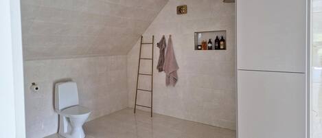 Een badkamer met toilet, douche, handdoekhouder en een plank met toiletartikelen.