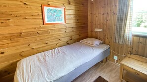 Een enkel bed met een kussen in een houten kamer, met een lijstfoto aan de muur.