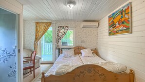 Une chambre avec un lit en bois, une chaise, une fenêtre avec des rideaux et un tableau accroché au mur.