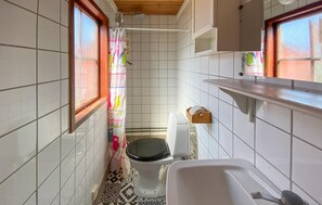 Une petite salle de bain avec des carreaux blancs, des toilettes, un lavabo et une fenêtre avec un rideau.