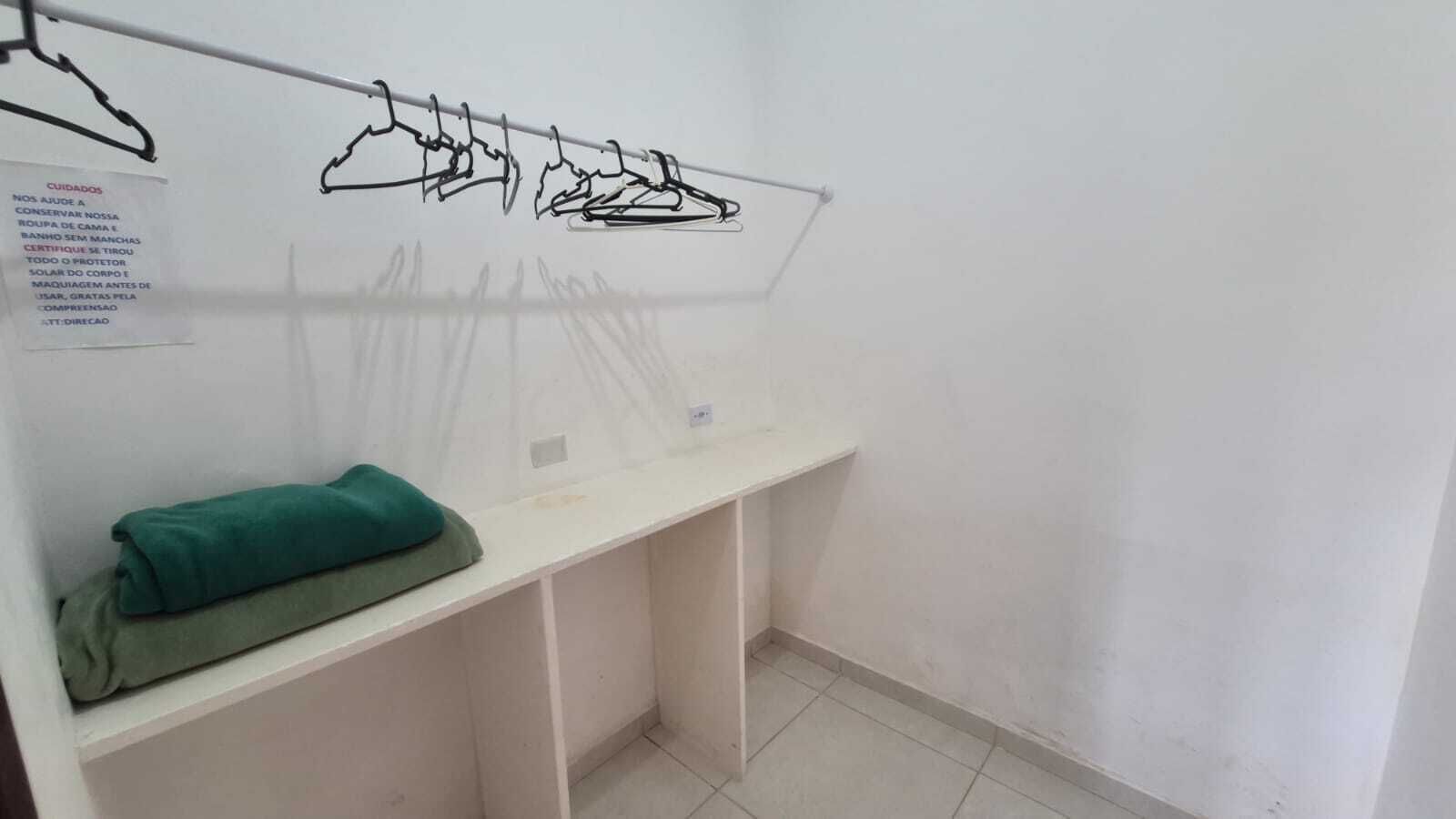 A room with a white desk, a green towel, and a clothes rack with hangers.