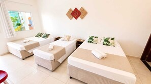 A hotel room with three single beds, a small table, and a view of the outdoors.