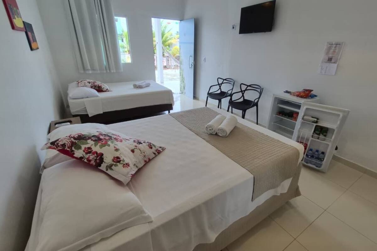 Habitación de hotel con dos camas, un televisor, una pequeña mesa con sillas y un dispensador de agua.