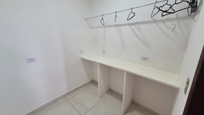 A room with a white wall, a white shelf, and a coat rack with hangers.