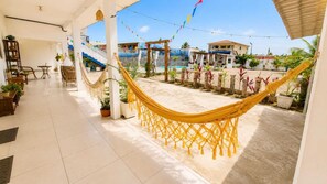 A hotel corridor with a hammock, potted plants, and a view of the pool and buildings. - Sonho Nosso Pousada (Maragogi)