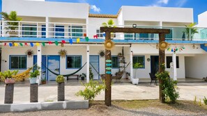 A building with a white facade, blue doors, and a balcony. There are potted plants and hammocks.