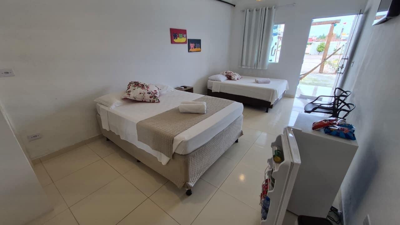 Habitación de hotel con dos camas, una mesita, una silla y una ventana con cortinas.