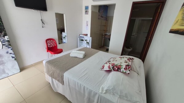 A bedroom with a bed, a red chair, a white wardrobe, a mirror, and a television on the wall.