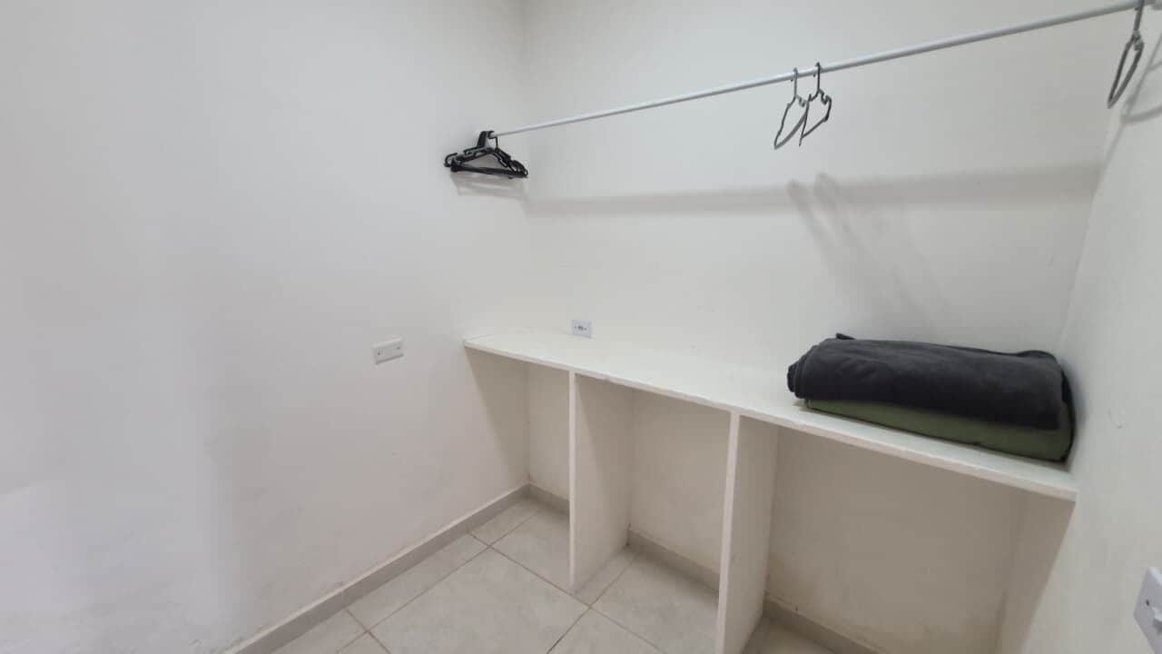 A small, white-walled room with a single white shelf and a black towel on it.