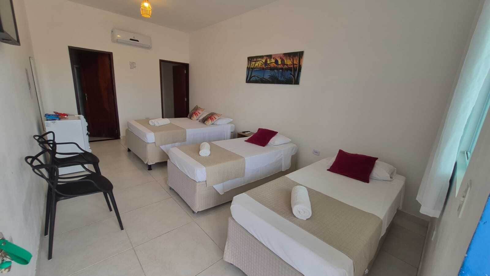 Quarto de hotel com três camas, uma escrivaninha e uma cadeira.