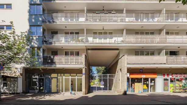 Un edificio residenziale a più piani con balconi, un ingresso a livello strada e un negozio visibile al piano terra.