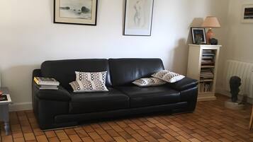 A living room with a black leather sofa, two framed artworks, a lamp, and a radiator.