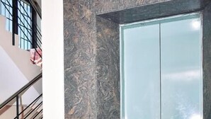 A staircase leading to a room with a glass elevator door, a marble wall, and a red carpeted floor.