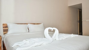 A neatly made bed with white linens and a heart-shaped towel arrangement.