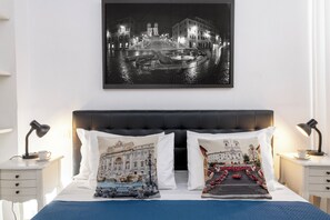 A hotel room with a bed, two nightstands, a lamp, a cup, and a framed black and white cityscape photo on the wall. - San Francesco Ripa Apartments (Roma)