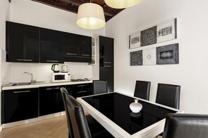 A modern kitchen with black cabinets, a white countertop, a dining table with chairs, and decorative wall art. - San Francesco Ripa Apartments (Roma)