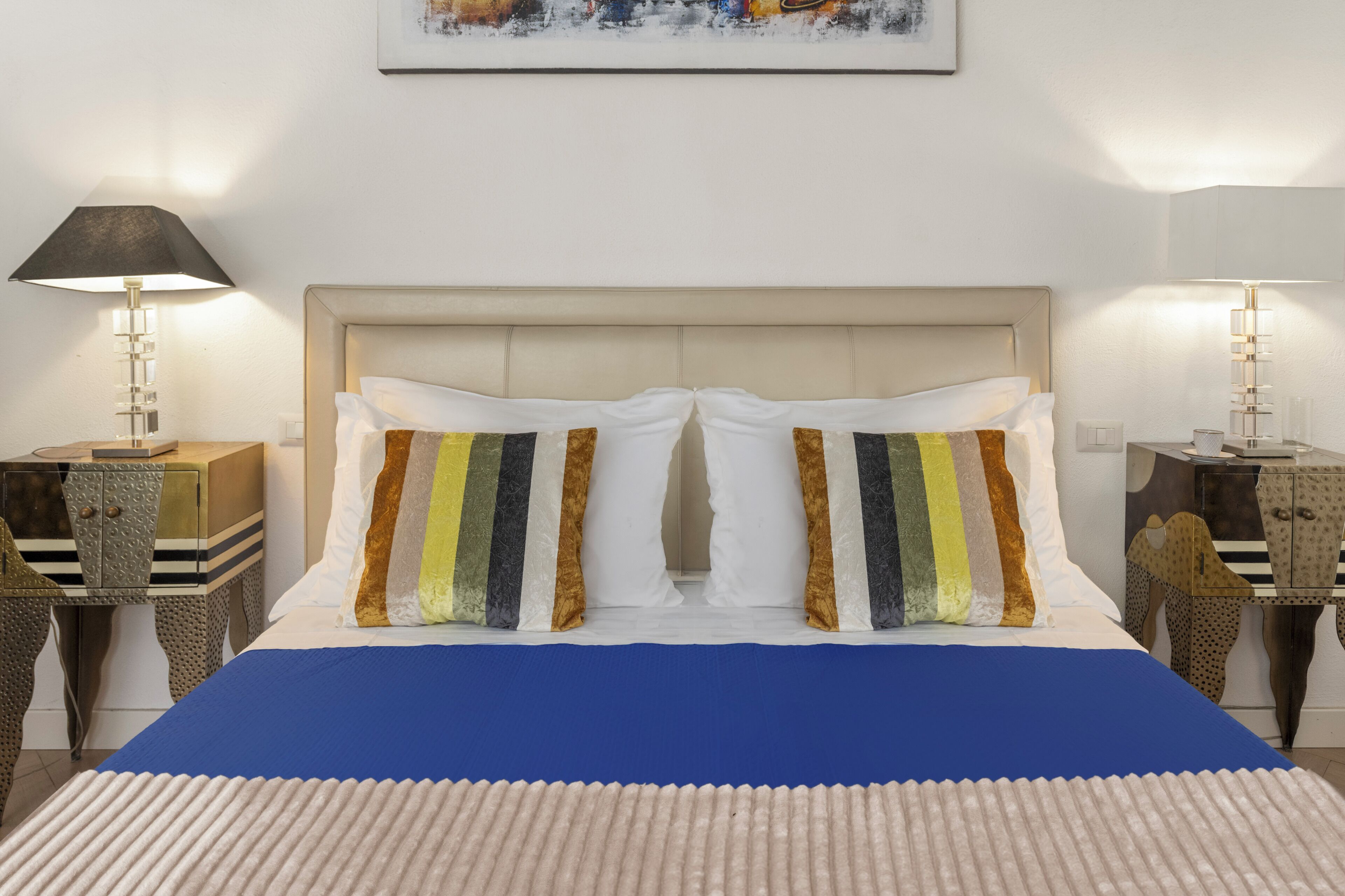 A hotel room with a large bed, two bedside lamps, a framed artwork on the wall, and a decorative headboard.