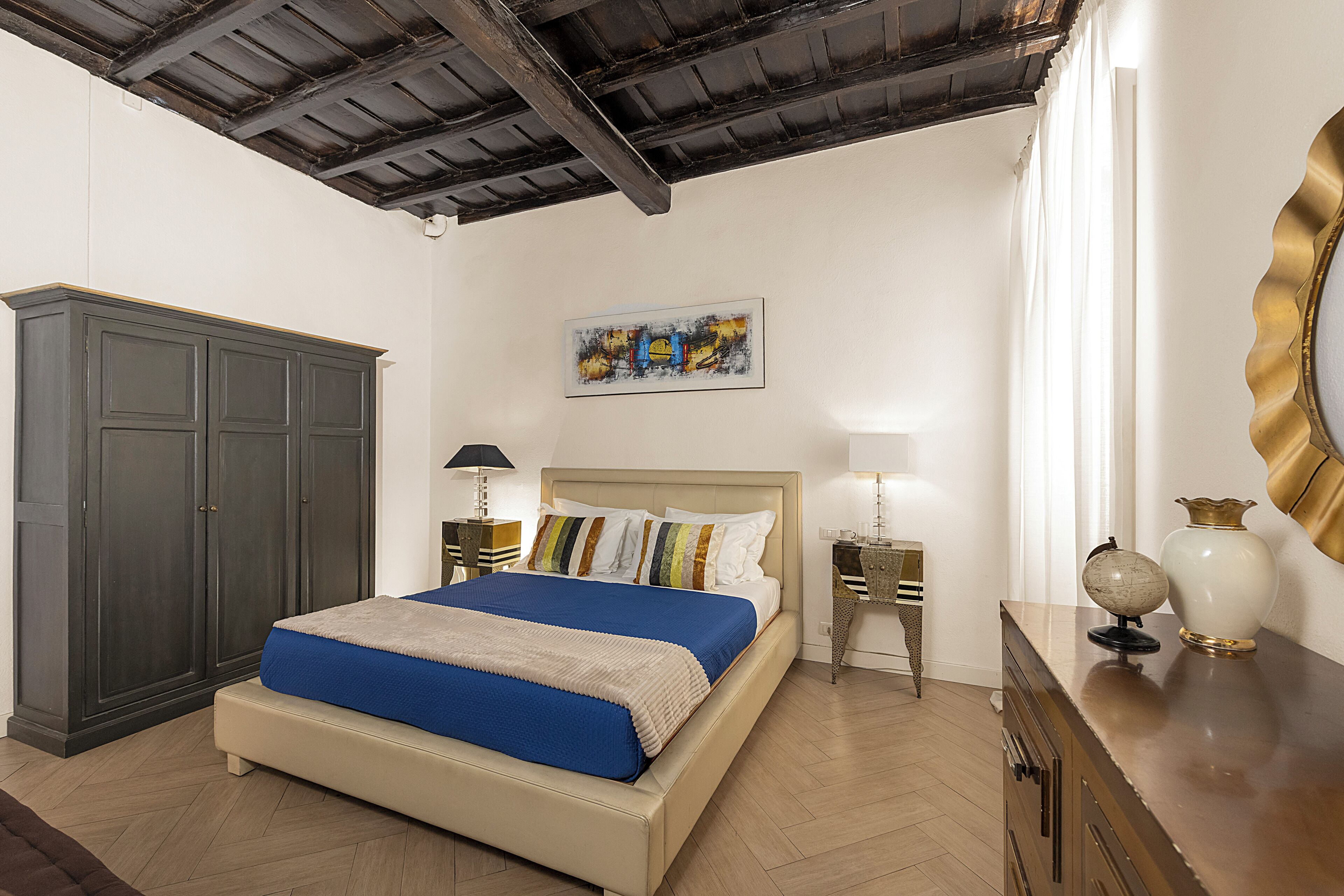 A hotel room with a bed, wardrobe, bedside tables, and a painting on the wall.
