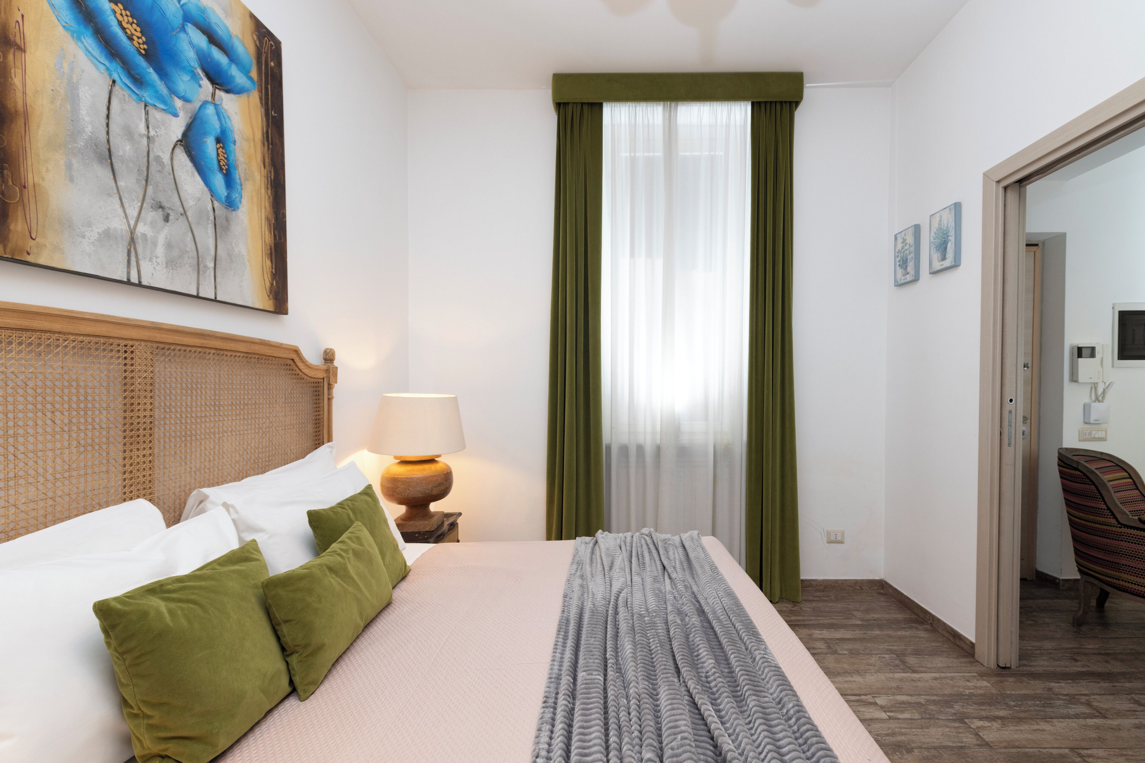 A hotel room with a bed, a lamp, a painting, and a view of the outside.