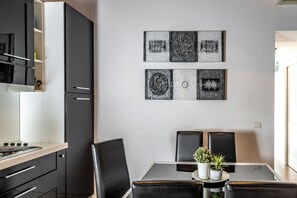 A modern kitchen with black cabinets and a dining area with a glass table and black chairs. - San Francesco Ripa Apartments (Roma)