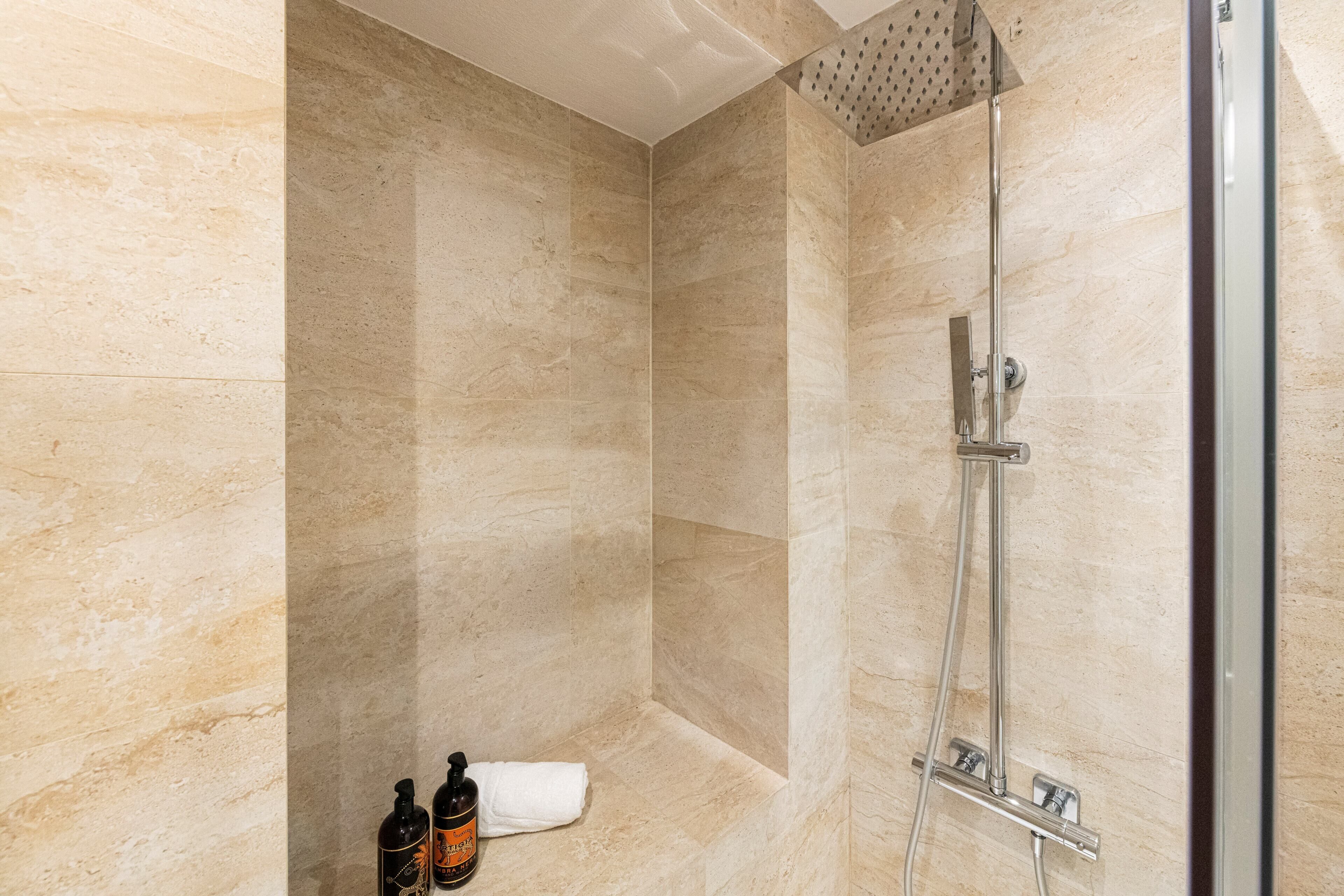 Un baño moderno con cabina de ducha de vidrio, paredes de mármol y un perchero con botellas.