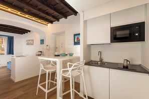 A modern kitchen with white cabinetry, a black microwave, a stainless steel sink, and two white bar stools. - San Francesco Ripa Apartments (Roma)