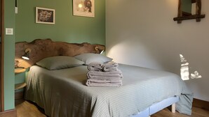 A bedroom with a wooden headboard, a bed with a checkered bedspread, two wall-mounted lamps, and a stack of folded towels.