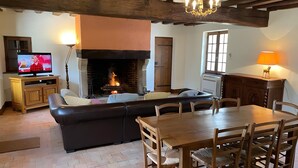 A cozy living room with a fireplace, a television, a dining table, and a sofa.