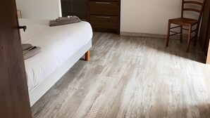 Quarto com cama, uma cadeira de madeira, um banheiro pequeno com pia e espelho, e uma escada que leva a um andar superior.
