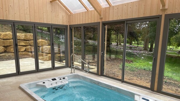 Uma piscina interior moderna com paredes de vidro, uma parede de pedra e um teto de madeira.