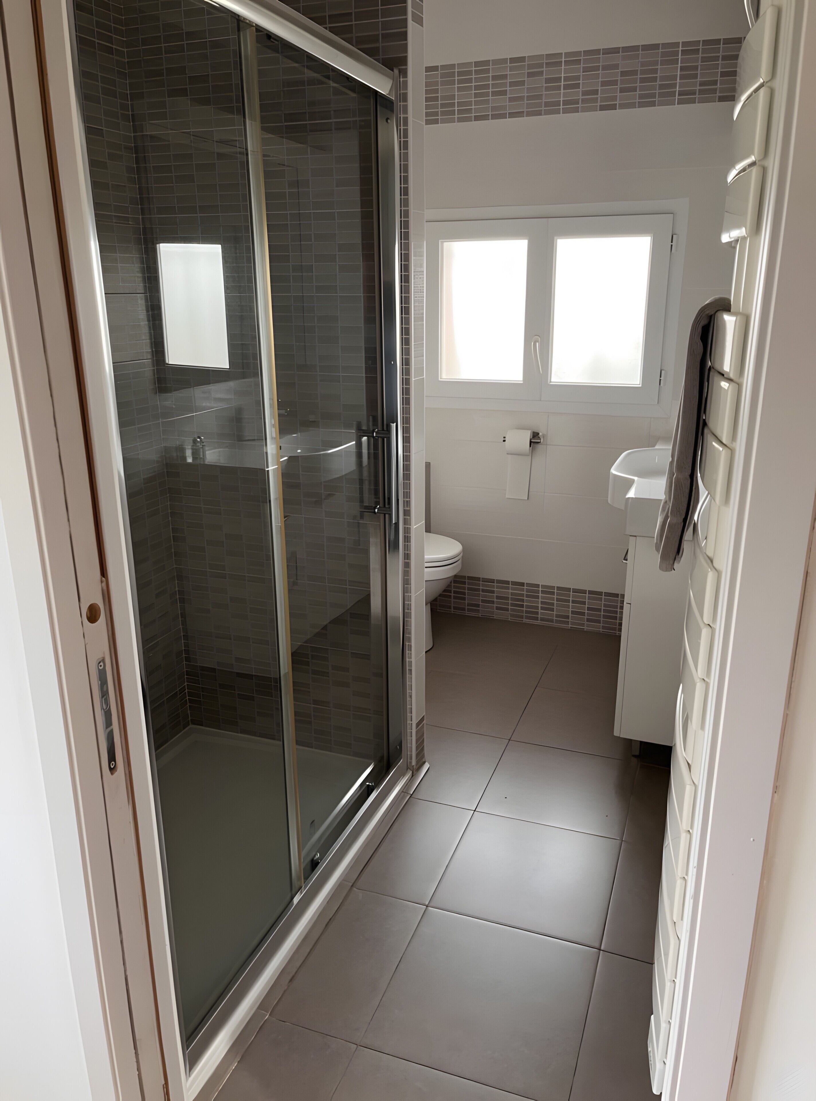 Ein Badezimmer mit Duschabtrennung, Toilette, Waschbecken und Fenster.