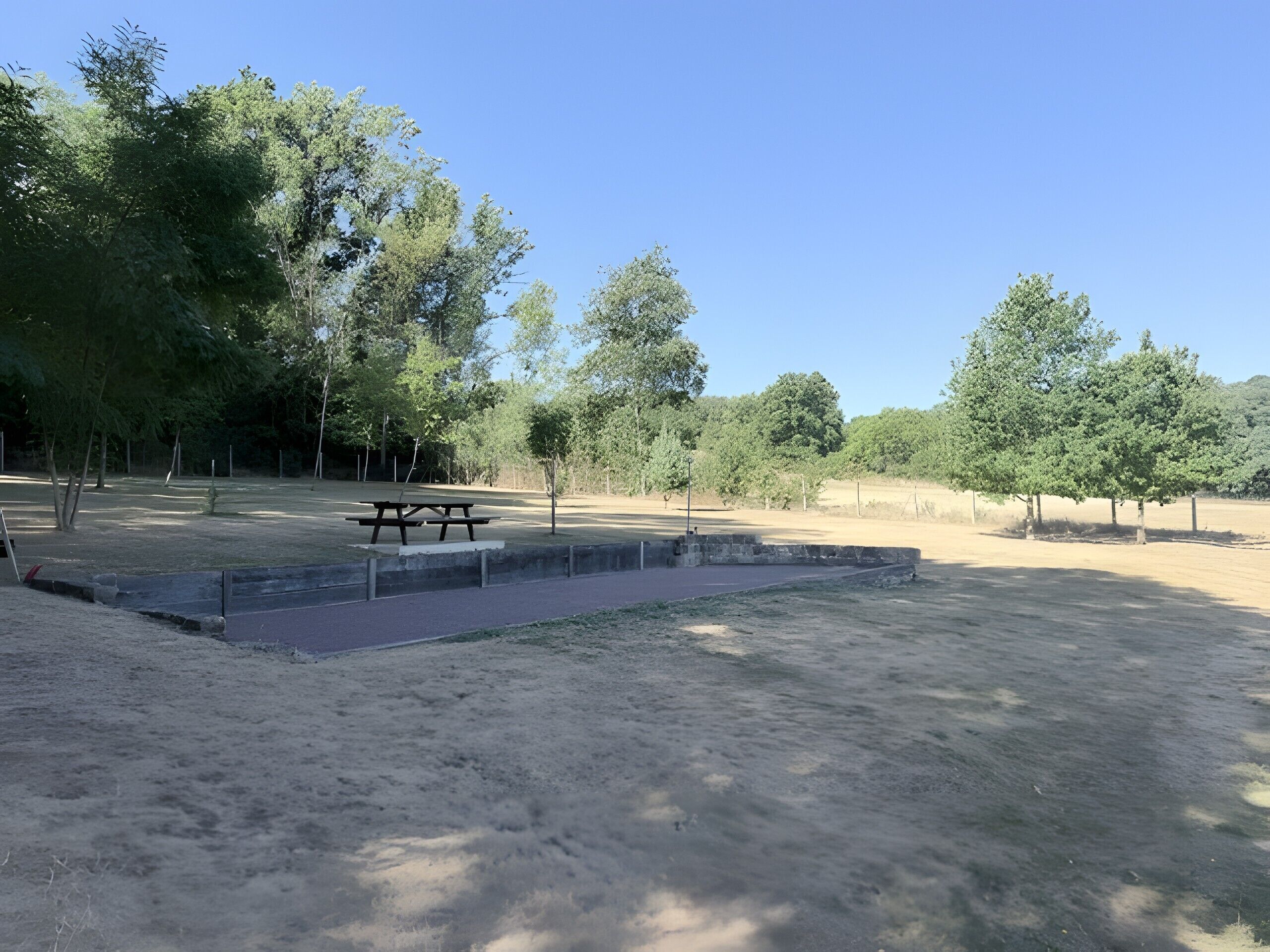 A park with a picnic table and benches, surrounded by trees and open grassy areas.