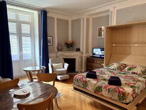 A hotel room with a bed, a chair, a table, a fireplace, and a television. - 36-square-meter studio apartment in the heart of downtown, with a balcony (Aix-les-Bains)