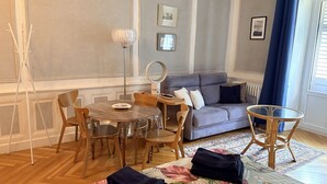 Ein Zimmer mit Esstisch, Stühlen, einer Couch, einem kleinen runden Tisch und einem Bett mit Blumenmuster.