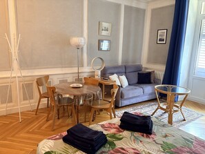 A room with a dining table, chairs, a sofa, a small round table, and a bed with a floral bedspread. - 36-square-meter studio apartment in the heart of downtown, with a balcony (Aix-les-Bains)