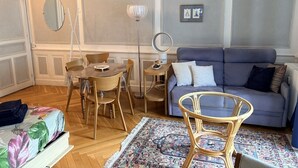 Ein Wohnzimmer mit einer Couch, einem Esstisch mit Stühlen, einer Stehlampe und einem Spiegel.