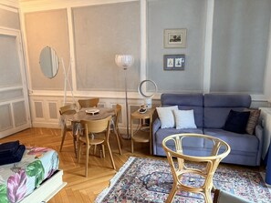 A living room with a sofa, a dining table with chairs, a floor lamp, and a mirror. - 36-square-meter studio apartment in the heart of downtown, with a balcony (Aix-les-Bains)