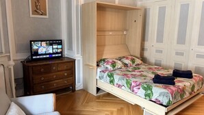 Ein Zimmer mit einem Bett, einem Holzschrank, einem Fernseher und einer Tür.