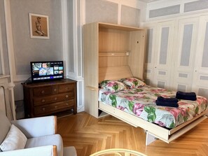 A room with a bed, a wooden dresser, a television, and a door. - 36-square-meter studio apartment in the heart of downtown, with a balcony (Aix-les-Bains)