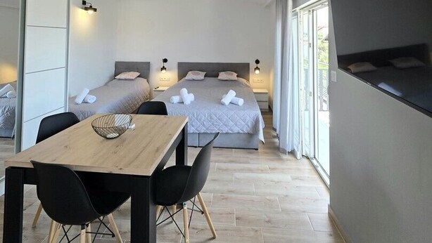 Ein modernes Hotelzimmer mit einem großen Bett, einem Fernseher, einem Esstisch und Blick ins Freie.