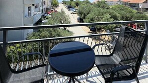 Ein Balkon mit Tisch und Stühlen mit Blick auf eine Straße, gesäumt von parkenden Autos und Gebäuden.