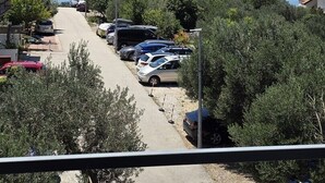 Eine Küstenstraße mit parkenden Autos, Bäumen und freiem Blick auf das Meer und die Berge in der Ferne.