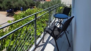 Un balcon avec une table et des chaises, une rambarde en métal, et une vue sur un parking et des bâtiments en arrière-plan.