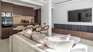 A modern kitchen with dark wooden cabinets, a dining area with a round table and chairs, and a large flat-screen TV mounted on the wall. - Luxurious Apartment - Croisette/hotel Mondrian (Cannes)