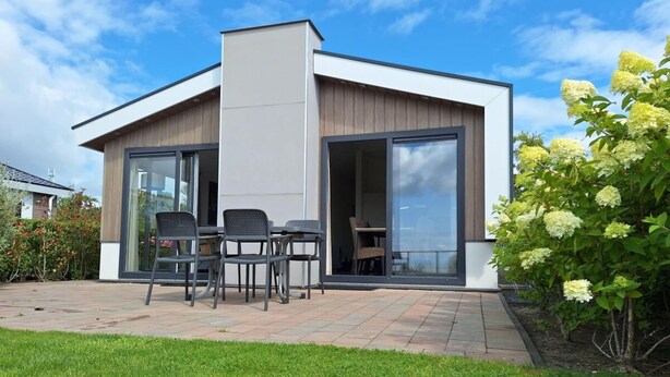 A modern house with a patio, a table with chairs, and a large sliding glass door. - Pavilion Waterfront 6 (Bovenkarspel)