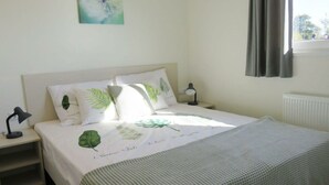 A bedroom with a bed, two bedside tables, a lamp, a window with curtains, and a wall-mounted artwork. - Pavilion Waterfront 6 (Bovenkarspel)