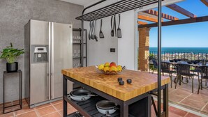 A kitchen with a wooden countertop, hanging utensils, a fruit bowl, and a view of the ocean. - Spacious 5-bedroom villa with Top views and heated pool in charming Benalmádena (Benalmádena)